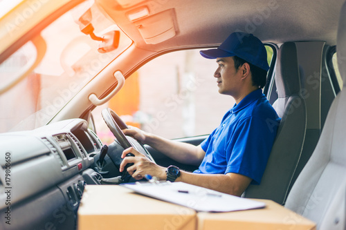 Young handsome delivery man driving his van with packages on the front seat