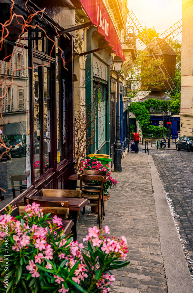 Naklejka premium Przytulna ulica ze stołami kawiarni i stary młyn w dzielnicy Montmartre w Paryżu, Francja