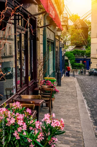 Obraz Przytulna ulica ze stolikami kawiarni i starym młynem w dzielnicy Montmartre w Paryżu, Francja