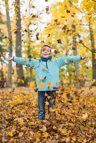Adorable happy kid playing with fallen leaves in autumn park © ventura