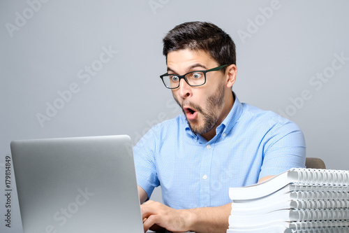 Young shocked man in blue shirt using laptop