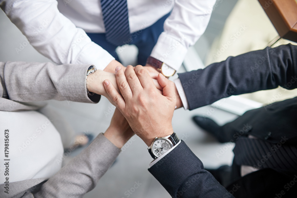 Group of colleagues in formalwear joining hands together while celebrating completion of joint project, close-up shot Group of colleagues in formalwear joining hands together while celebrating completion of joint project, close-up shot