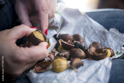 Mädchen mit roten Fingernägeln schält Kastanien ab, Kastanien und Schalen auf Zeitungspapier am Knie, Nahaufnahme