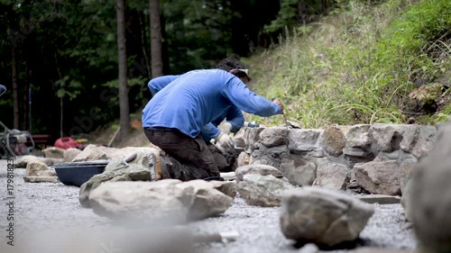 Using a tuckpointing trowel a hardscape smooths out the mortar in a rock wall being built. photo