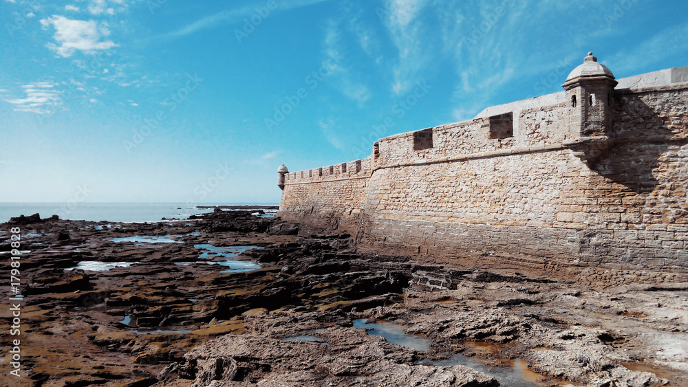 Fortress of San Sebastian, low tide and stones covered with algae on a sunny day in Cadiz, Andalusia, Spain.