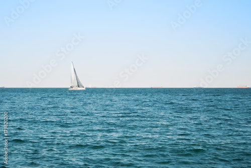 Sea lake ocean water landscape with dark waves and a lonely white yacht at the horizon on sunny day. © Victoria