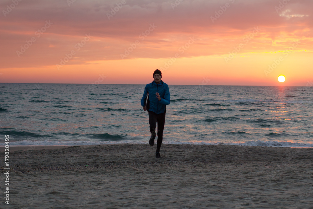 young man in atumn clothes training on the beach, sunrise background, male runner at morning  