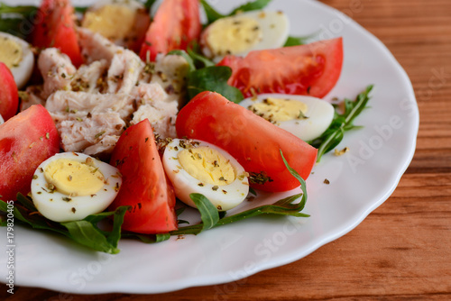 Homemade vegetable chicken salad for lunch or dinner. Healthy salad with fresh tomatoes, rocket, quail eggs, chicken fillet and spices on a white plate and a wooden background. Closeup