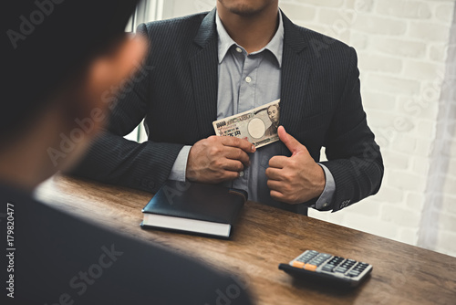 Businessman putting money, Japanese Yen banknotes, into his suit pocket