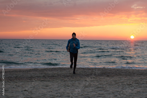 young man in atumn clothes training on the beach, sunrise background, male runner at morning 