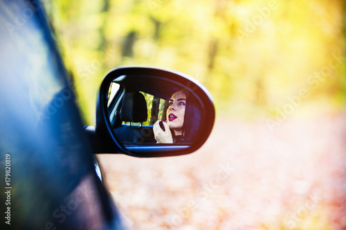 a beautiful woman sitting in the car and applying a lipstick in the mirror