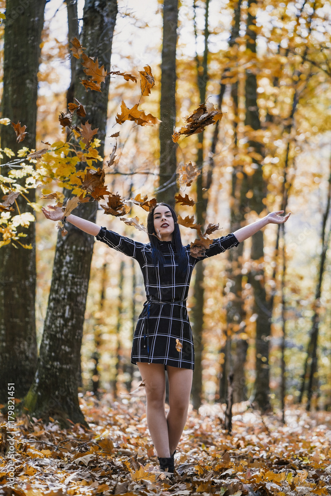 the brunette girl throwing the leaves upwards enjoying the autumn