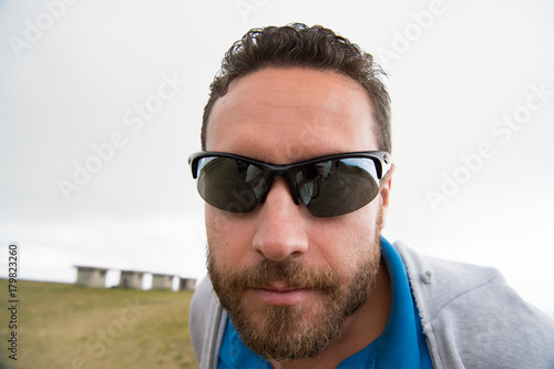 Man with unshaven face, beard and mustache in black sunglasses
