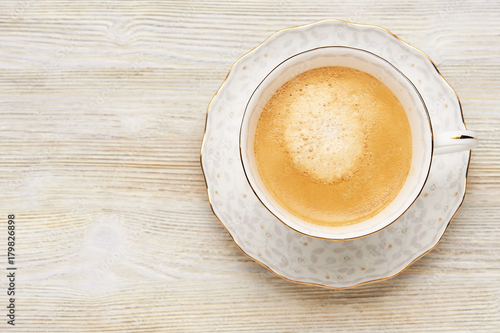 Top view of cappuccino coffee in a bright white Cup on a wooden light table. Top view of cappuccino coffee in a bright white Cup on a wooden light table.