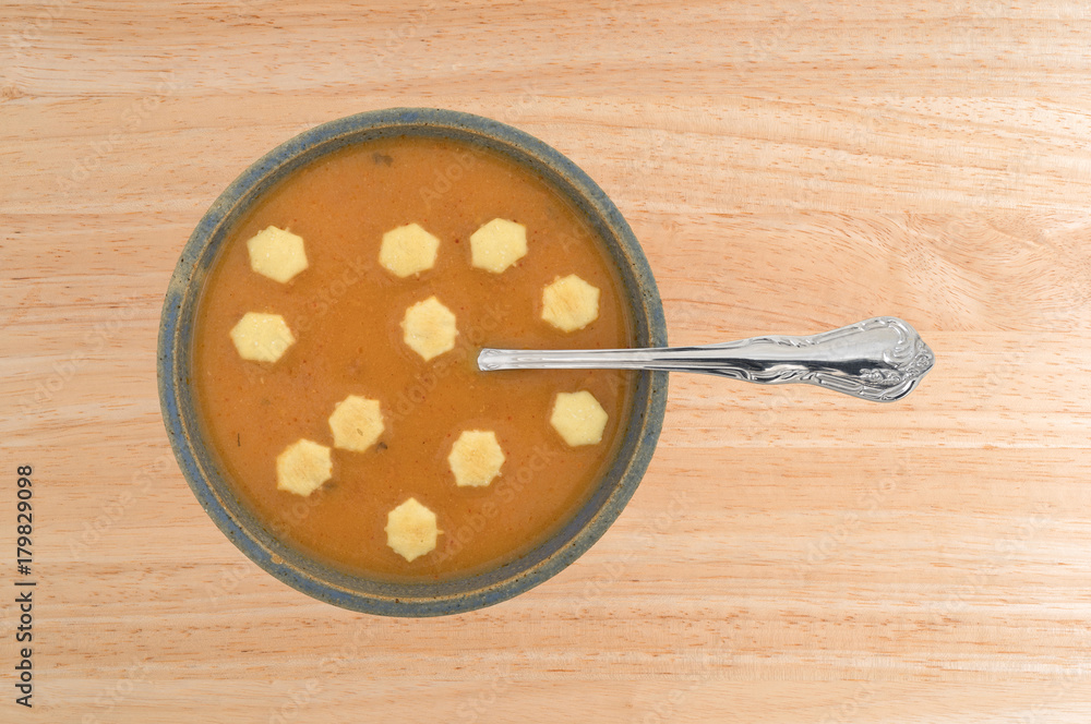 A serving of salmon bisque soup in an old stoneware bowl with a spoon in the food plus several crackers on a wood table top. A serving of salmon bisque soup in an old stoneware bowl with a spoon in the food plus several crackers on a wood table top.