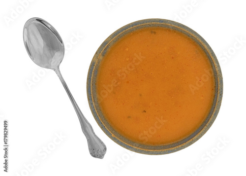 Top view of a serving of salmon bisque soup in an old stoneware bowl with a spoon to the side isolated on a white background.