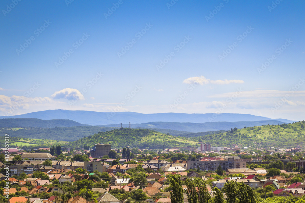 Beautiful summer landscape with city, mountains and cloudy blue sky