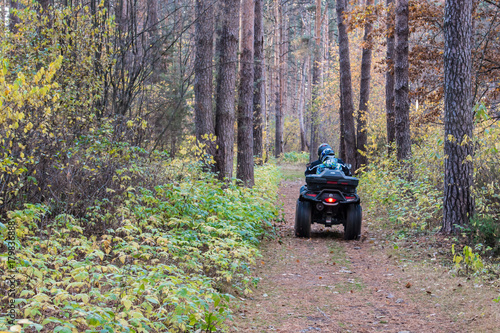 ATV quad with driver and passenger on magic picturesque path in the autumn forest