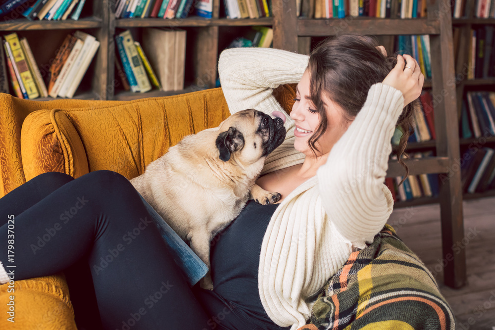 Happy funny dog licking a girl sitting on the chair in library. Lovely pet and owner friendship