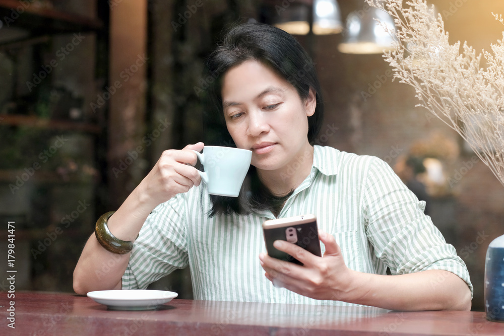 Asian woman using smart phone and drinking coffee while sitting by window cafe background, People technology and lifestyle Asian woman using smart phone and drinking coffee while sitting by window cafe background, People technology and lifestyle