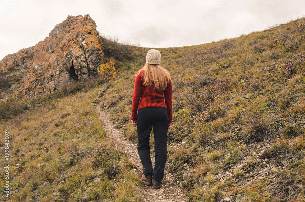 Naklejka premium A girl in a red jacket walks in the mountains, an autumn forest with a cloudy day, free space for text