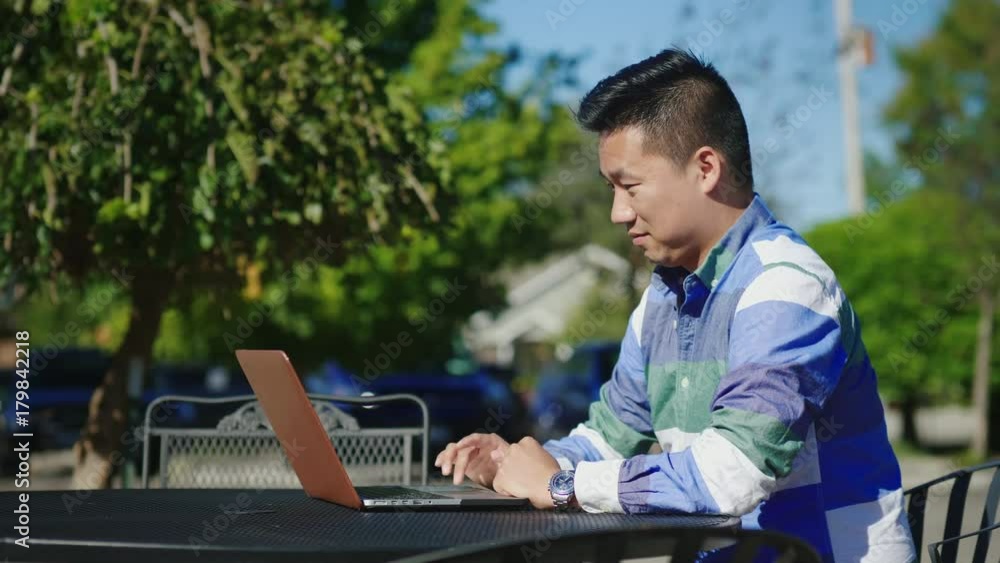 Young Chinese man working with laptop. On the summer terrace in the cafe Young Chinese man working with laptop. On the summer terrace in the cafe