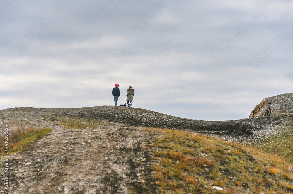 The guy with the girl stand on the mountain in the autumn cloudy day.
