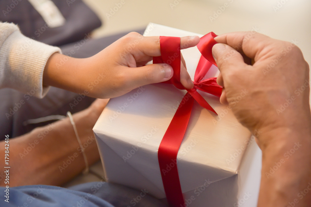 Asian boy and elderly man holding on red ribbon of white gift box. Asian boy and elderly man holding on red ribbon of white gift box.