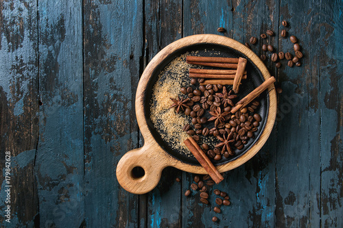 Ingredients brown sugar, coffee beans, cinnamon sticks, anise on wooden serving board. Over old dark blue wooden background. Top view with space
