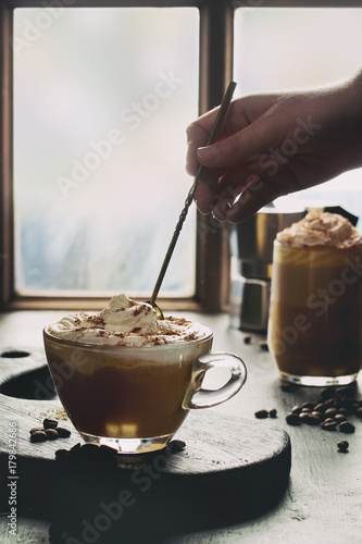 Bilde på lerret Glass of spicy pumpkin latte with whipped cream and cinnamon standing wooden serving board on cafe table near window with coffeepot and coffee beans above