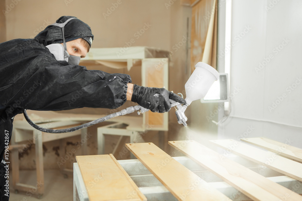 Man in respirator mask painting wooden planks at workshop. Man in respirator mask painting wooden planks at workshop.