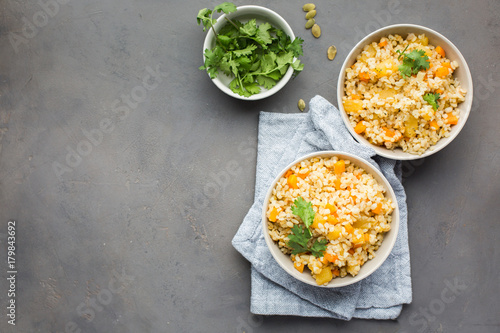 The perfect vegetarian dinner. Bulgur with pumpkin, carrots, spices (ginger, cinnamon, pepper, cardamom), honey and cilantro. A autumn gray concrete background for you. Flat lay, top view