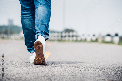 Close up woman wear jean and white sneaker walking forward on highway road in sunny day,Alone travel or solo traveler concept photo