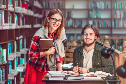 Portrait of two successful students casual stylish, boy and girl in library reading hall, evening time, education concept