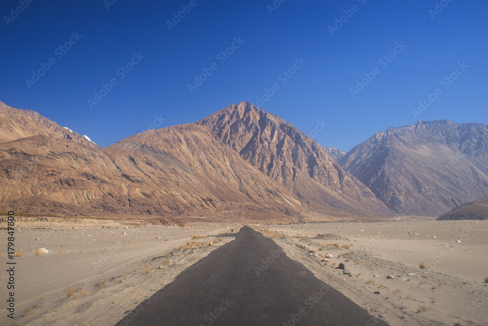 Straight road to mountains with blue sky background