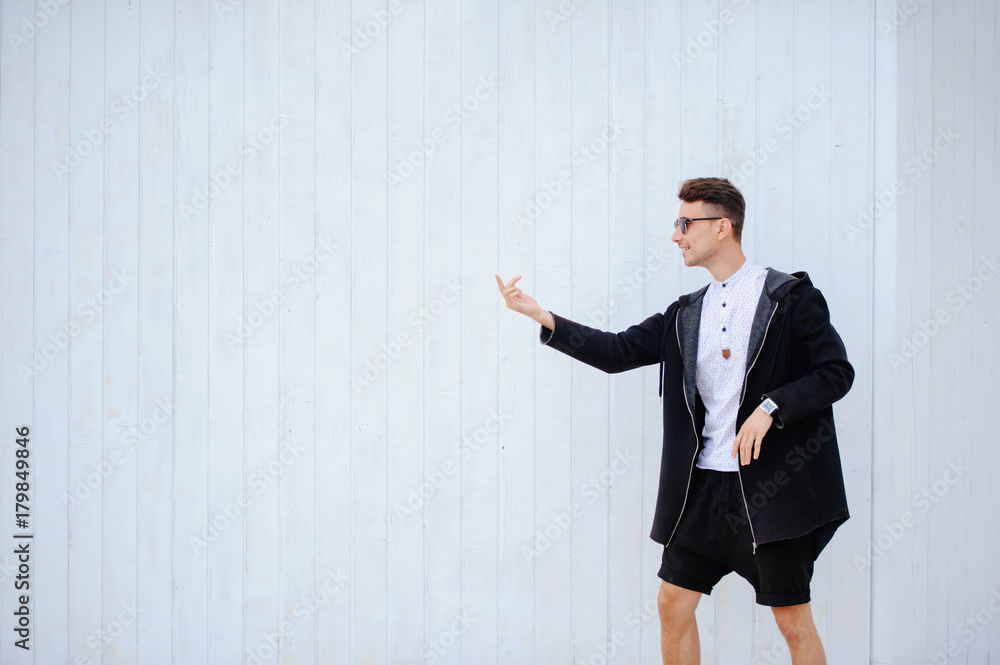 fervent fashionable man on a white wall. Raises his hands to the left of the frame. dressed in a shirt and black shorts. left side for text fervent fashionable man on a white wall. Raises his hands to the left of the frame. dressed in a shirt and black shorts. left side for text