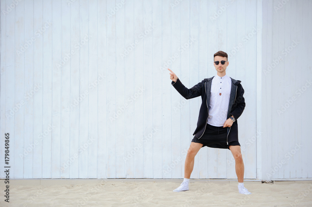 fervent fashionable man on a white wall. Raises his hands to the left of the frame. dressed in a shirt and black shorts. left side for text fervent fashionable man on a white wall. Raises his hands to the left of the frame. dressed in a shirt and black shorts. left side for text