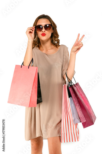 Shopper woman in dress with shopping bags shows two fingers and sends air kiss.