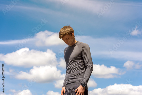 Portrait of healthy athletic man with fit body, resting after workout or running. Thirsty male with a drink after outdoor training. sports, fitness concept. Sky background. © Wisiel