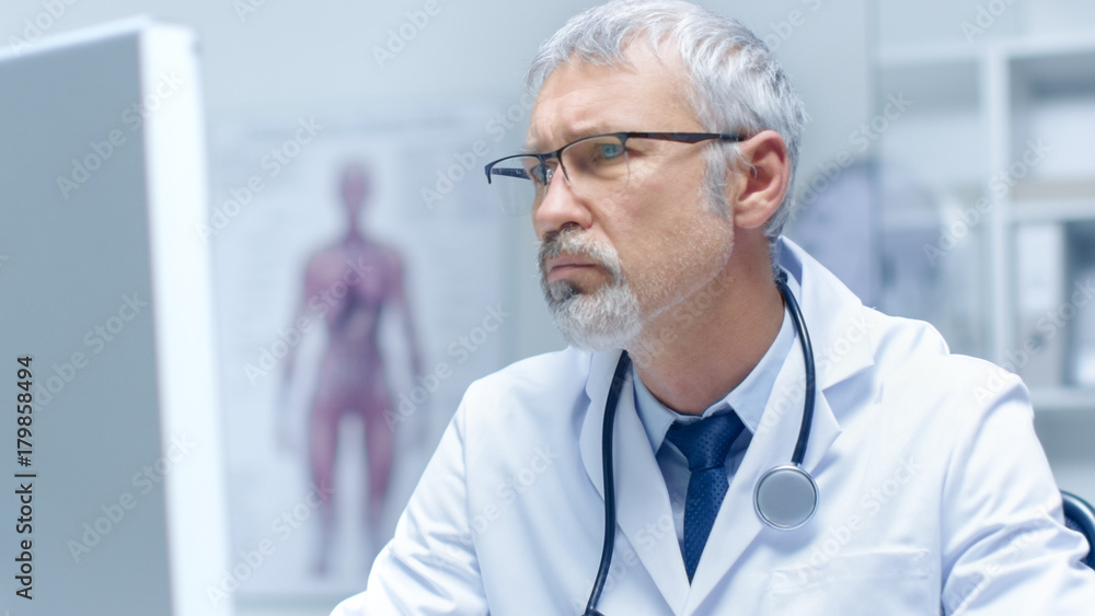 Close-up Portrait of a White Haired Doctor Working on Personal Computer. His Office is Bright and Light. Close-up Portrait of a White Haired Doctor Working on Personal Computer. His Office is Bright and Light.