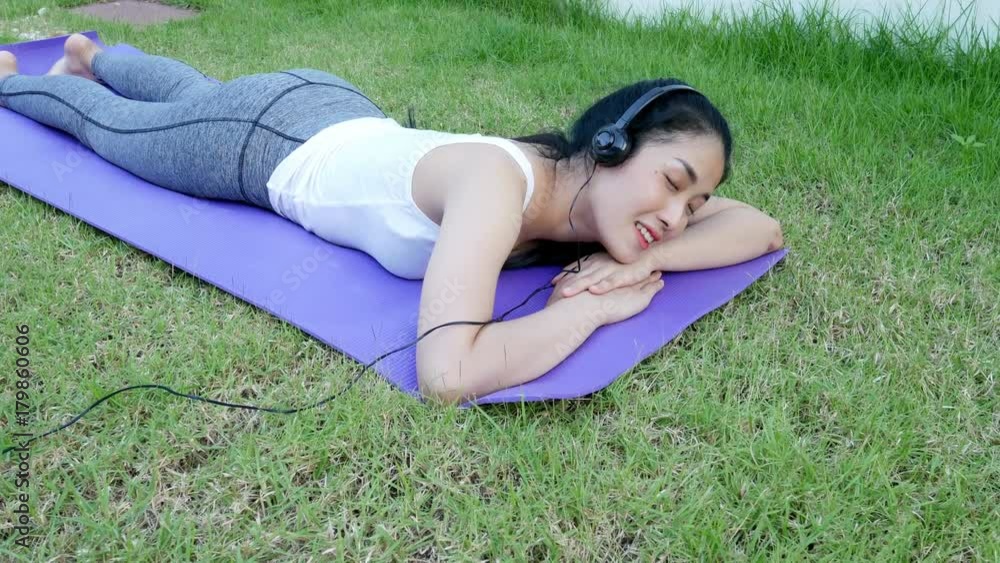 4k of Young woman lying on grass in Park, listening to music on headphones on a mat 4k of Young woman lying on grass in Park, listening to music on headphones on a mat