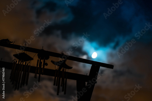 Fotografia Chime bells hanging from an old well in the night sky - Silhouettes of chime bell in the moonlight