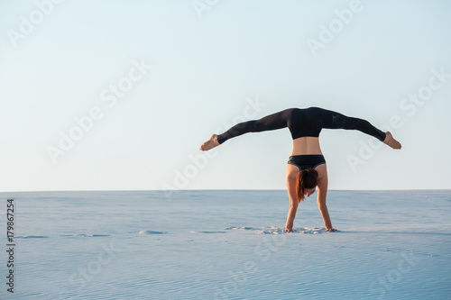 Young woman practicing inversion balancing yoga pose handstand on sand.