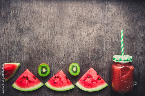 Watermelon fresh smoothie in glass jar, slices of watermelon on a dark wooden background