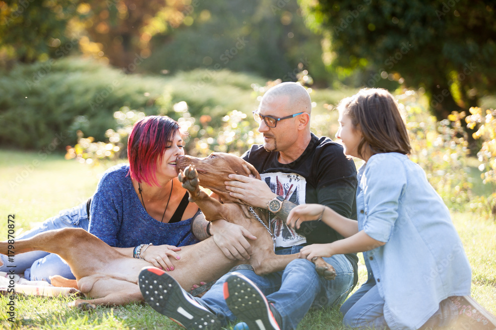 Beautiful gorgeous family of three playing in the park with their dog. Animal lovers. Mother, father, daughter and their dog Beautiful gorgeous family of three playing in the park with their dog. Animal lovers. Mother, father, daughter and their dog