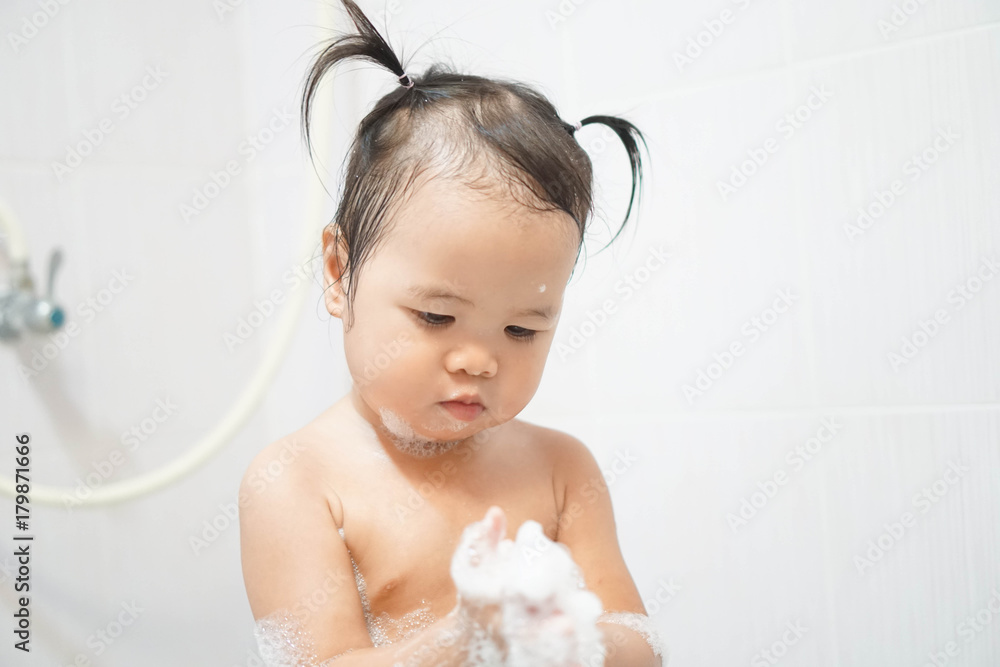 Little asian girl taking shower in bathroom, playing bath foam bubbles