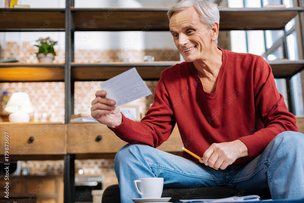 Positive mood. Cheerful nice happy man holding the note and looking at it while being in the positive mood Positive mood. Cheerful nice happy man holding the note and looking at it while being in the positive mood