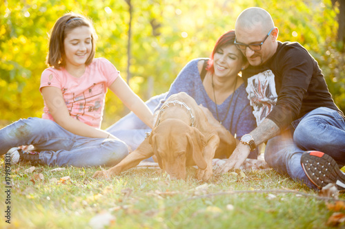 Beautiful gorgeous family of three playing in the autumn park with their dog. Animal lovers. Mother, father, daughter and their dog