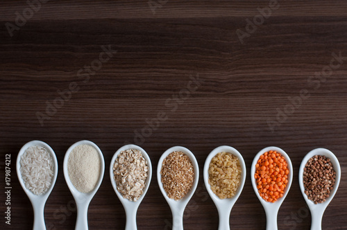 An even row of cereals in the same white dishes on a dark wooden background