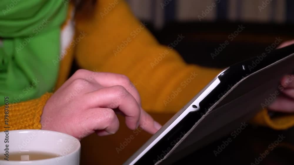 Young girl sitting in cafe at table and uses a tablet computer. Hands close-up. Young girl sitting in cafe at table and uses a tablet computer. Hands close-up.